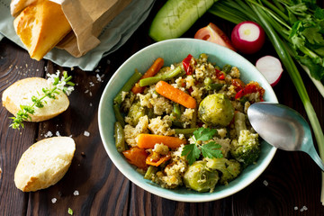 Healthy proper nutrition. Homemade vegetarian couscous with string beans, brussels sprouts, carrots, sweet peppers and tomatoes on a dark rustic wooden kitchen table.