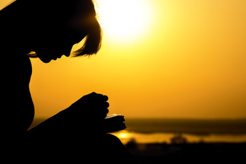 silhouette of the hands of woman praying to God in the nature witth the Bible at sunset, the...