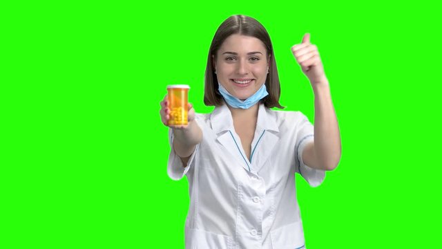 Can of pills and thumb up. Teen breunette girl working as doctor and promote medicines. Green screen hromakey background for keying.