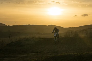 Naklejka na ściany i meble Motorcyclist riding off road during sunset. Slovakia