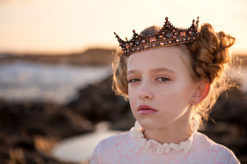 Portrait of a young capricious princess in the rays of the rising sun in the crown