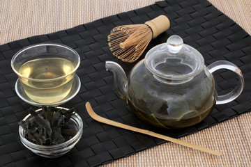 Japanese sencha wakame seaweed  tea with glass teapot and cup, dried leaves, stirrer and whisk on bamboo background. Has many health benefits and is very high in minerals.