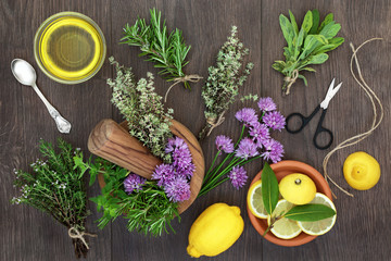 Fresh herb seasoning selection in a mortar with pestle and loose with lemon fruit and olive oil on rustic wood background. Top view.