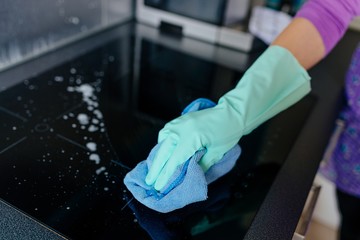 Young woman in rubber gloves cleaning modern induction cooker