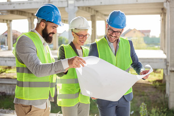Mixed group of smiling engineers or business partners at construction site, working together on...