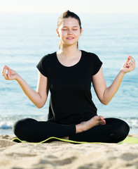 Smiling adult woman in black T-shirt is sitting and practicing asana