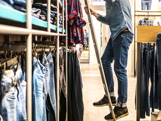 man picking jeans in the clothes store on the ladder