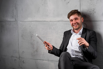 Young smiling businessman have relax break with smartphone and tablet,  portrait on grey wall background copy text.