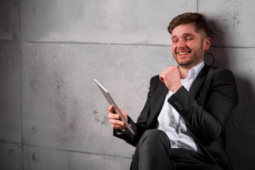 Young handsome businessman in suit with tablet and beaming smile on face, close-up portrait on grey wall background