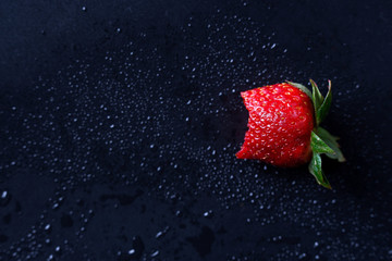 A bitten strawberry on a dark background.