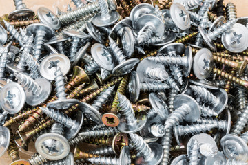group of silvery self-tapping screws is arbitrarily positioned on a wooden surface, selective focus, abstract background