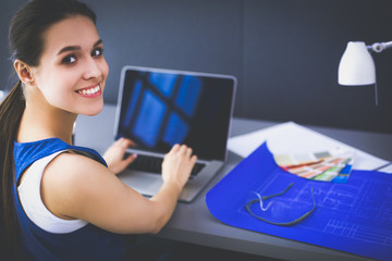 Young woman sitting at the desk with instruments, plan and laptop