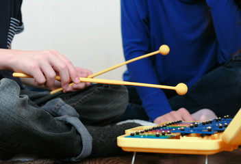 Playing music instrument. Closeup boy's hand playing on xylophone and his mom sitting near him.