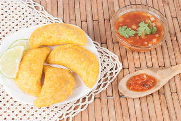Colombian empanada with spicy sauce on wooden background