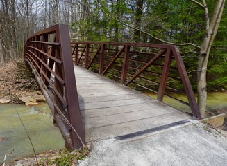 Red metal and wooden bridge over a creek on a nature trail.