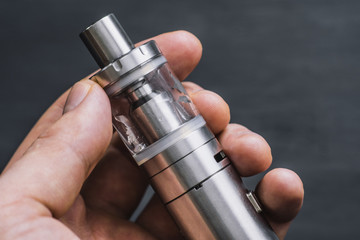 man holding electronic cigarette or vape device with smoke at the background.