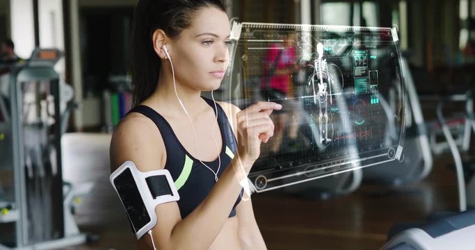 Futuristic portrait of a beautiful girl in the gym on a stationary bike uses a hologram to strengthen her body and heart heartbeat and pressure Concept future of humanity,new technology futuristic gym