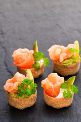 Croustades  crispy pastry cases filled with salted salmon and avocado on black stone background