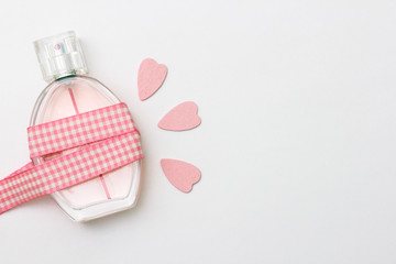 Bottle of parfume, pink hearts, plaid ribbon and place for a simple text on a light white background.