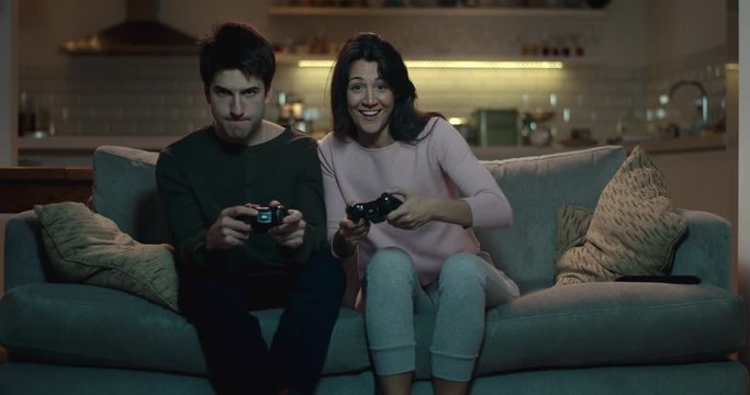 Competitive couple push and shove each other as they play a video game at home
