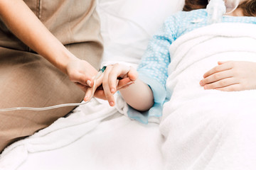Mother holding little girl hand with IV saline intravenous in hospital