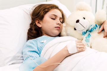 Sick little girl sleeping on the bed with medication through intravenous  in hospital