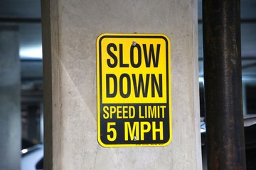 Yellow and Black Slow Down Speed Limit 5 Mph Sign in a Parking Garage with Cars Out of Focus in the Background