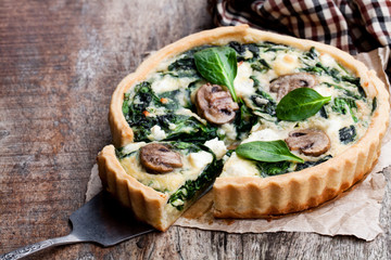 Traditional  french quiche pie with spinach and mushroom on wooden table