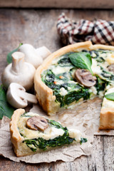 Traditional  french quiche pie with spinach and mushroom on wooden table