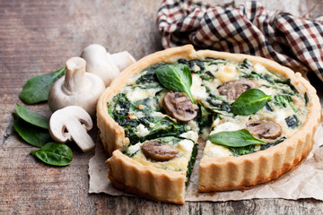Traditional  french quiche pie with spinach and mushroom on wooden table
