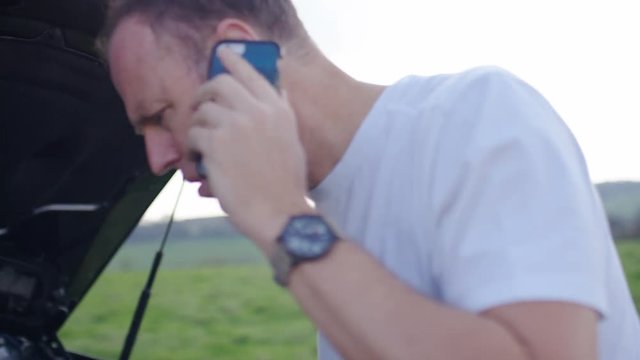 Middle aged man on his phone as he checks what's wrong his broken down vehicle