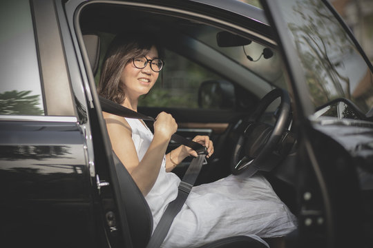 asian woman sitting in driver seat of sedan car fasten safety seat belt