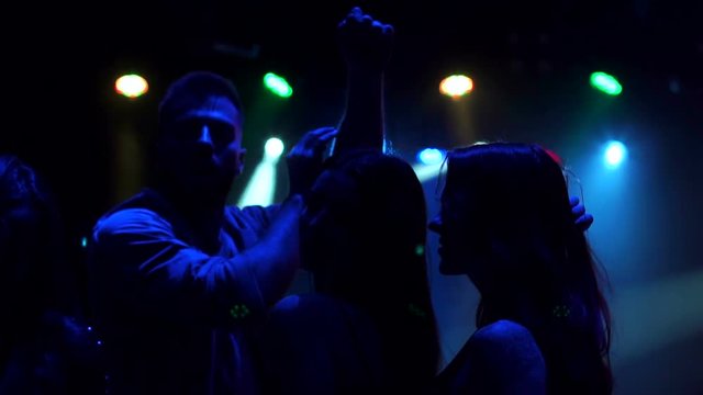 Close-up of a group of girls and guys dancing in the dark at a disco with bright concert lighting. Silhouette. Slow motion.