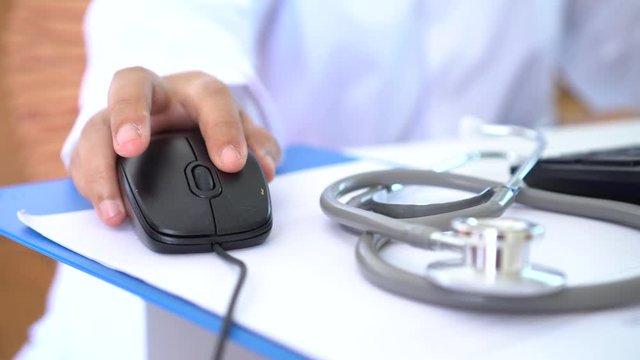Healthcare and medical concept: Medicine doctor's working and using mouse on laptop computer with Stethoscope on prescription clipboard on workplace in hospital, Focus on stethoscope