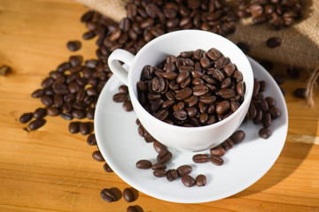 Roast coffee beens in a cup on wooden table.