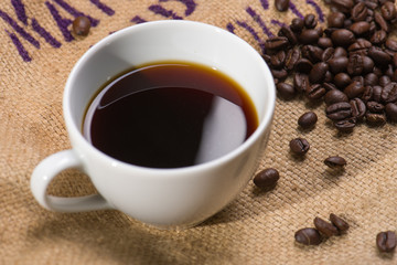 A cup of black coffee with beans on wooden table.