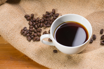 A cup of black coffee with beans on wooden table.