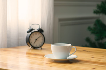 A cup of coffee and a pot of plants on a wooden table by the window. Focus on cup.