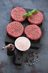 Black wooden cutting board with raw fresh beef burger cutlets ready to be cooked, vertical shot