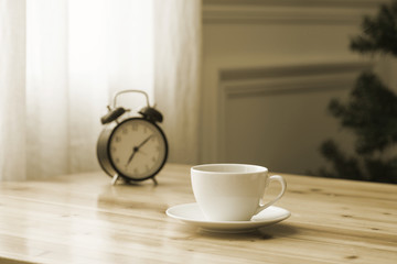 A cup of coffee and a pot of plants on a wooden table by the window. Focus on cup.