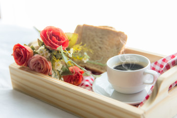 Fresh morning coffee with bread, rose in tray on the bed, early work day.  Lifestyle Concept