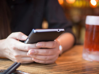 Happy young woman eating sushi in a restaurant and using mobile phone