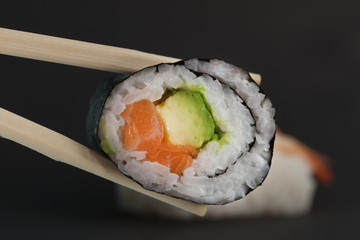 Close up of chop sticks holding a salmon avocado maki sushi