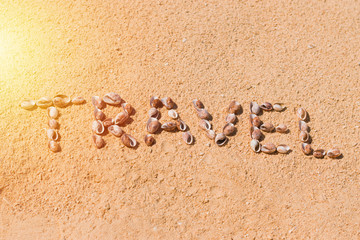 Vacation: word travel made with sea shells on a sand beach in the sun