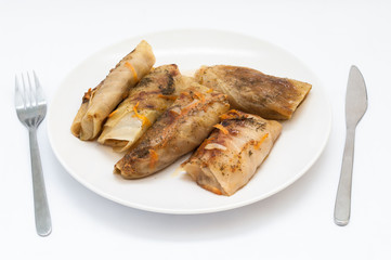 Tasty stuffed cabbage leaf laying on plate on isolated white background, fork and knife on both sides