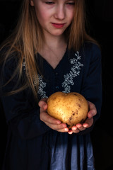 The young blonde girl holds  the big potato in the shape of heart in her hands