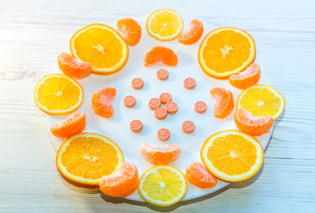 Vitamin C concept. Orange, tangerine and lemon slices and citrus fruit shape pills on a white plate.