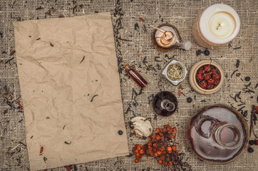 Herbal medicine background. Alternative medicine. Dry curative herbs and wild berry essential oil and blank crumpled paper page sheet (recipe, doctor prescription) on burlap sackcloth background.