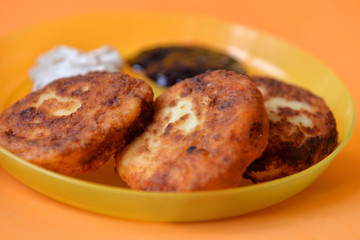 Cheesecakes from cottage cheese with sour cream and jam in a yellow plate on an orange background
