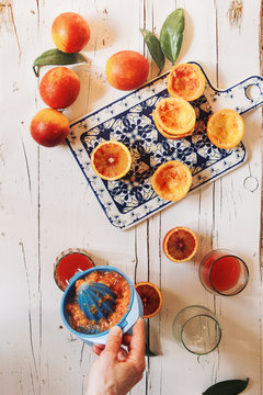 Woman's hand preparing blood orange juice over white wooden table